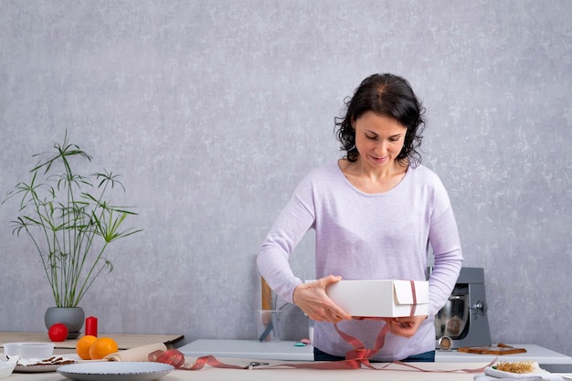 Vrouw verpakt cadeau in witte kartonnen doos met rood lint.