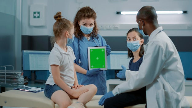 Vrouw verpleegster analyseren digitale tablet met groen scherm en arts legt diagnose uit. Assistent met Chromakey-achtergrond met geïsoleerde mockup-sjabloon en blanco kopieerruimte tijdens pandemie.