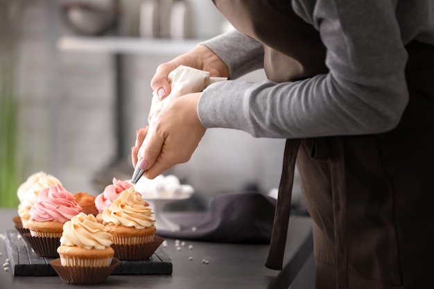 Foto vrouw versieren smakelijke cupcakes met slagroom aan tafel