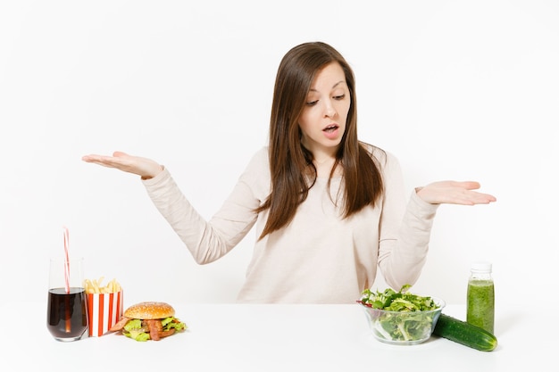 Vrouw verspreiding handen met groene detox smoothies, salade in glazen kom, komkommer, hamburger, cola in fles geïsoleerd op een witte achtergrond. goede voeding, gezonde levensstijl, fastfood, keuzeconcept.