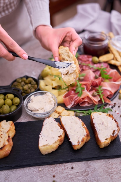 Vrouw verspreidt boter op gegrild stuk stokbrood met Italiaanse antipasto vleesschotel op achtergrond