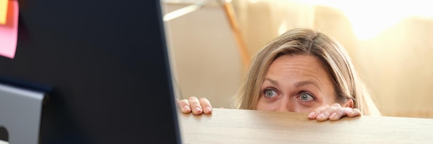 Foto vrouw verstopt zich achter bureau en kijkt naar computermonitor enge filmfout op het werk