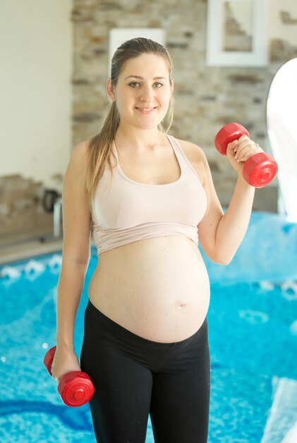 Vrouw verwacht baby die oefening met halters doet in de sportschool