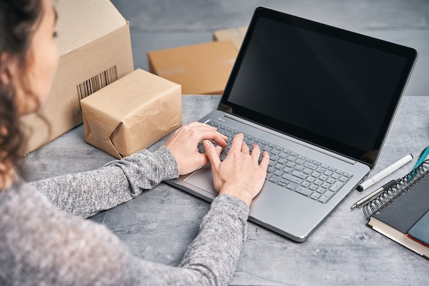 Vrouw verzendt pakket met haar laptop die vanuit huis werkt