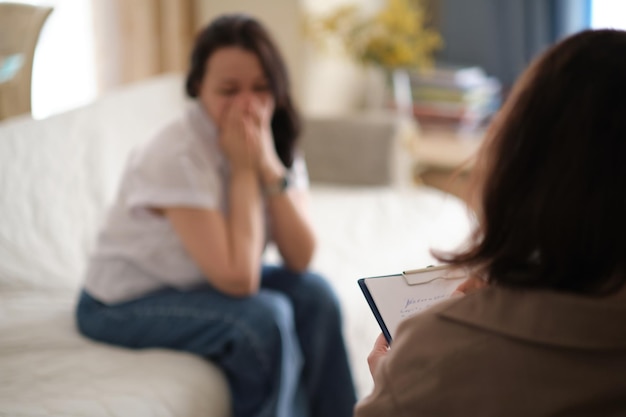 Vrouw vindt troost in het vertrouwen en de steun van haar therapeut tijdens een counselingsessie De psycholoog maakt aantekeningen om ervoor te zorgen dat de therapie vertrouwelijk blijft