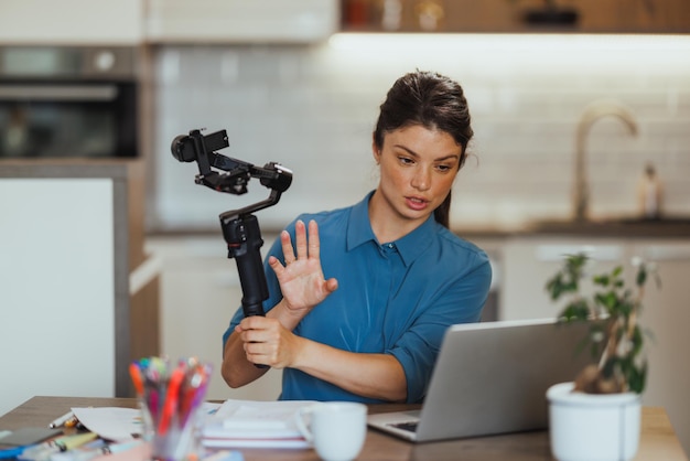 Foto vrouw vlogt over fotografische producten en toont gimbal voor de camera terwijl ze een online vergadering heeft vanuit haar kantoor thuis