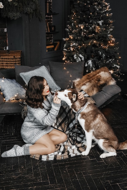 Vrouw voedt een hond bij de kerstboom.