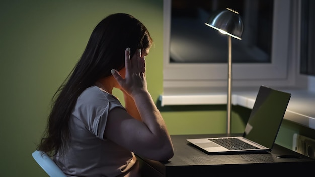 Vrouw voelt zich moe in de ogen door het werken op een laptop. Brunette vrouw wrijft in de ogen met vingers aan tafel met apparatuur in de buurt van vloerlamp