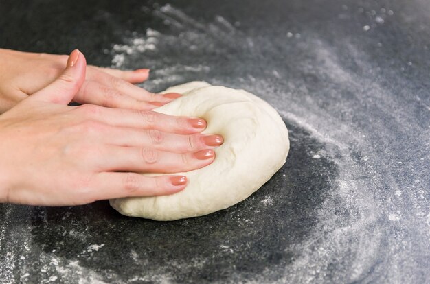 Vrouw voorbereiding van pizzadeeg op zwart granieten tafel