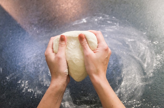 Vrouw voorbereiding van pizzadeeg op zwart granieten tafel