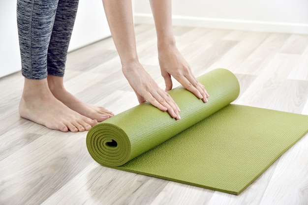 Vrouw vouwen yoga of fitness mat na thuis sporten, home training training.