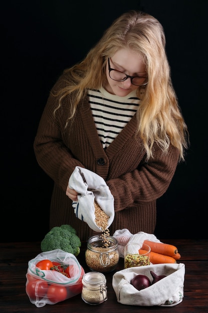 Vrouw vullen herbruikbare plastic gratis bank met korrels uit eco tas op houten tafel.