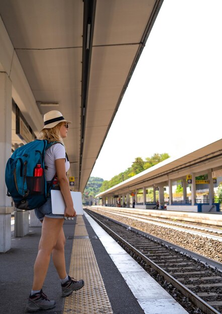 Vrouw wacht op de trein op het station terwijl ze graag werkt aan het concept van reizen en transport van digitale nomaden via de telefoon