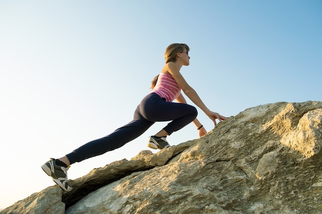 Vrouw wandelaar klimmen steile grote rots op een zonnige dag.