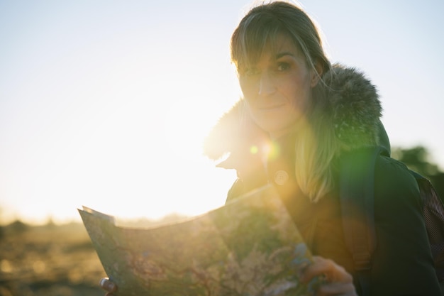 Vrouw wandelaar met een rugzak en een kaart in de juiste richting zoeken in de wildernis bij zonsondergang