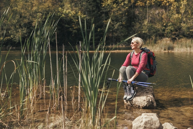 Vrouw wandelaar met rugzak zit alleen op een rots en geniet van het uitzicht op het meer in de bergen.