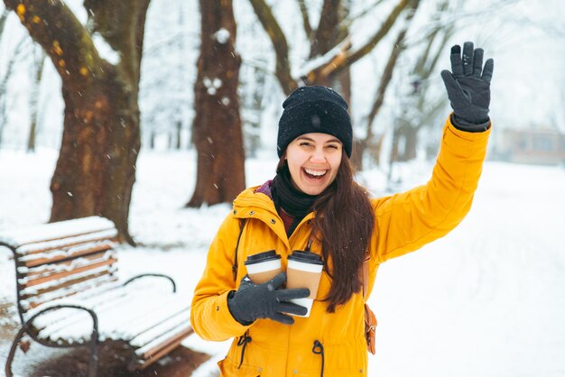 Vrouw wandelen door gesneeuwd stadspark met koffiekopje. opwarmen koude dag concept