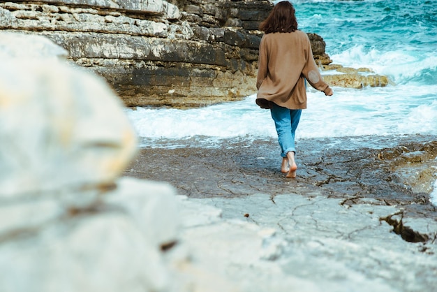 Vrouw wandelen door rotsachtige zee strand op zonnige winderige dag zomervakantie zorgeloos concept golven op background