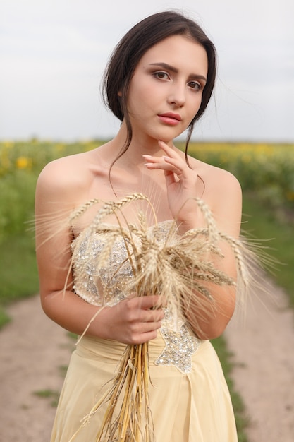 Vrouw wandelen in gouden gedroogd grasveld. Natuurlijke portretschoonheid. Mooi meisje dat tarweoogst in haar handen houdt terwijl ze in een geel tarweveld is