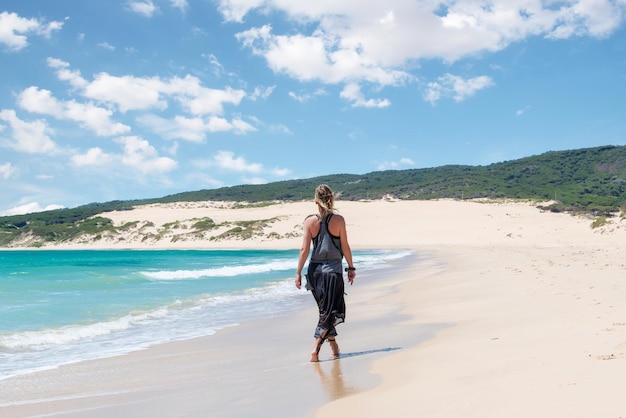 Vrouw wandelen langs de kust van het strand van Valdevaqueros in Tarifa, Spanje met een duin op de achtergrond