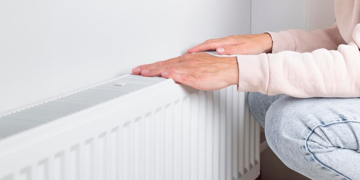Vrouw warmt haar handen bij de verwarmingsradiator bij huis resource management tijdens koudere seizoenen