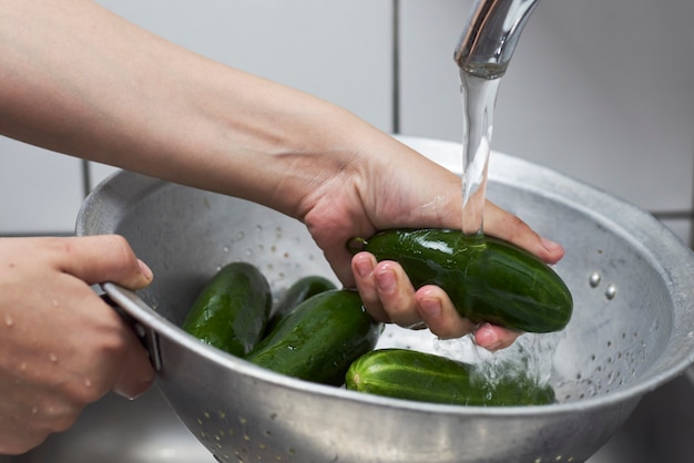 Vrouw wassen van vers geplukte biologische komkommers in vergiet