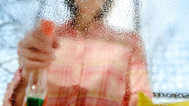 Vrouw wast een vensterglas van stof en vuil met behulp van een spray met wasmiddelen en vodden