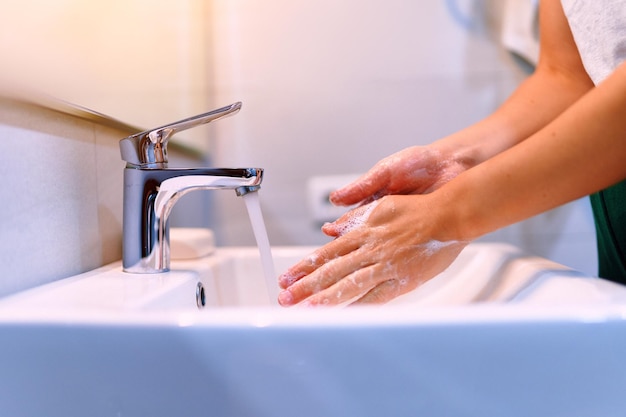 Vrouw wast haar handen met vloeibare desinfecterende zeep en stromend water in de badkamer close-up. Persoonlijke handhygiëne, gezondheidszorg