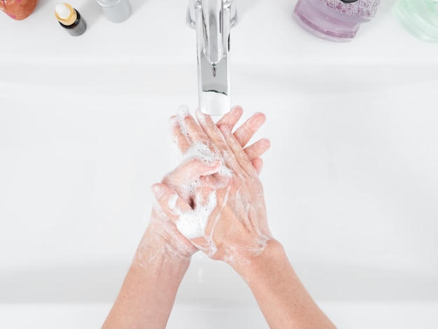 Vrouw wast haar handen met zeep onder een waterkraan in de badkamer. Hygiëne- en desinfectieproducten. Hygiëneconcept in detail. Bovenaanzicht, gezondheidszorg.