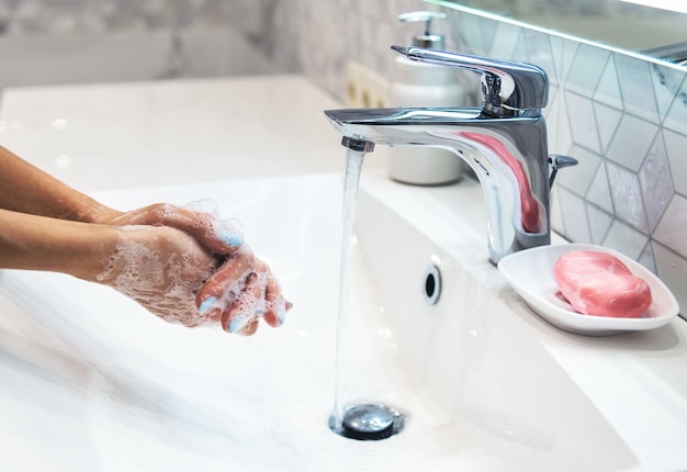 Vrouw wast handen met zeep en warm water thuis badkamer wastafel. Het meisje maakt handen schoon. Hygiëne voor preventie van coronavirusuitbraak. Covid-19 pandemische bescherming door regelmatig de handen te wassen