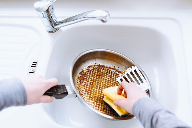 vrouw wast verbrande vettige koekenpan met keukenwashandje in gootsteen