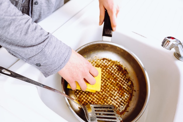 vrouw wast verbrande vettige koekenpan met keukenwashandje in gootsteen