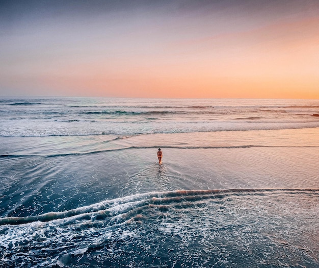 Vrouw watert in de zee tegen de hemel tijdens zonsondergang