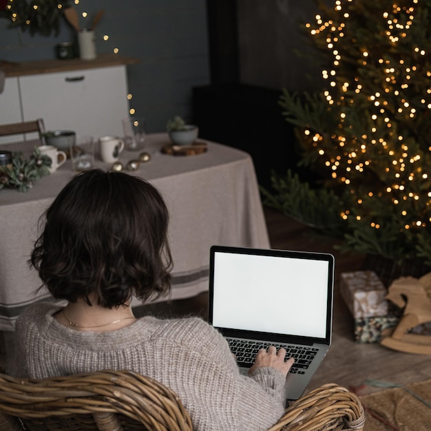 Vrouw werk op laptopcomputer met leeg scherm mockup kopie ruimte Modern huis woonkamer interieur ingericht voor kerstviering met kerstboom en slinger lichten