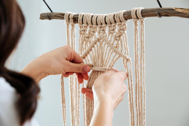 Vrouw werkt aan een macrame-stuk opgehangen aan een stok