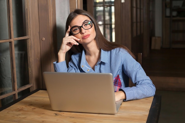 Vrouw werkt aan iets aan de houten tafel met grijze laptop