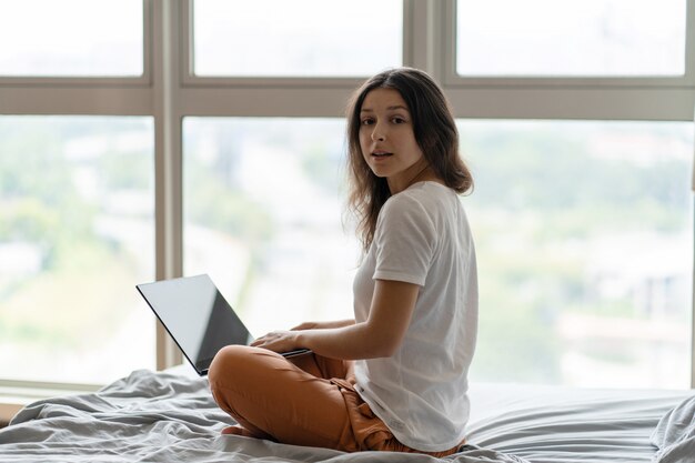 Vrouw werkt op de laptop zittend op een bed