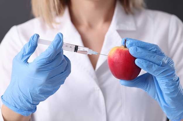 Vrouw wetenschapper in rubberen handschoenen injectie maken in apple close-up. Genetische manipulatie
