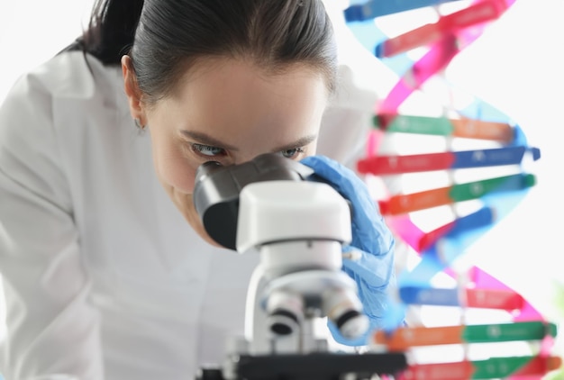 Foto vrouw wetenschapper kijkt door de microscoop in de buurt van dna-molecuul mockup in het laboratorium