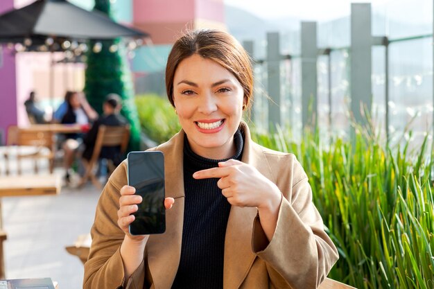 Vrouw wijst naar telefoon toont scherm naar camera glimlacht buiten achtergrond