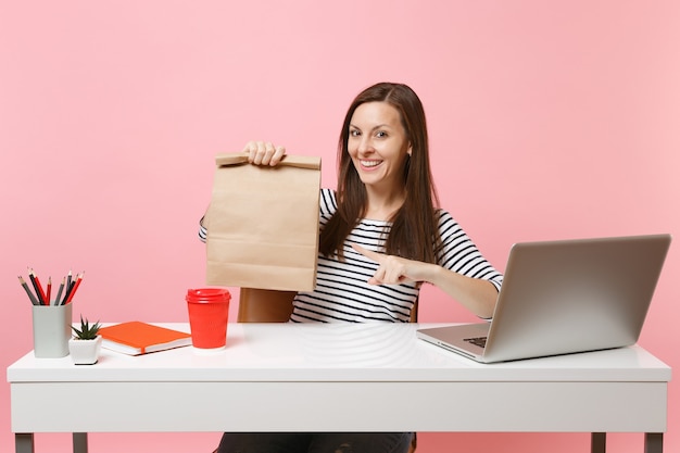 Vrouw wijzend op bruine doorzichtige lege lege ambachtelijke papieren zak, werk op kantoor met laptop with