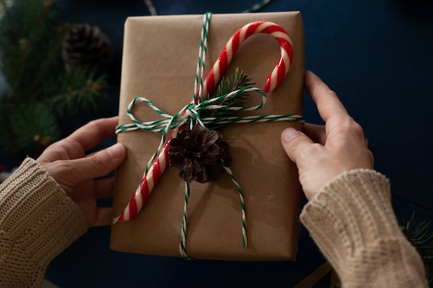 vrouw wikkelt een handgemaakt kerstcadeau in eco-stijl in kraftpapier en natuurlijke sparren takken op een blauwe houten achtergrond.