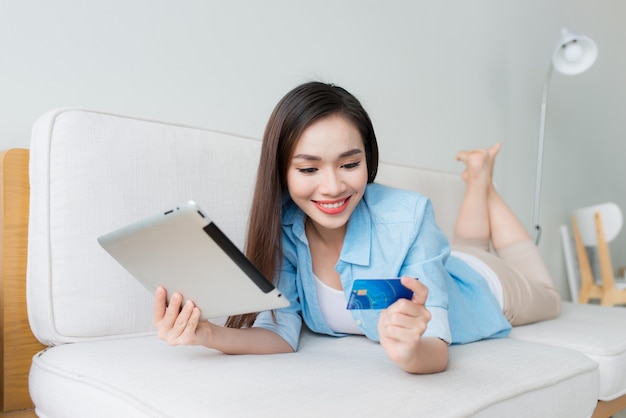 Vrouw winkelen op tabletcomputer en creditcard zittend op de bank glimlachend happy