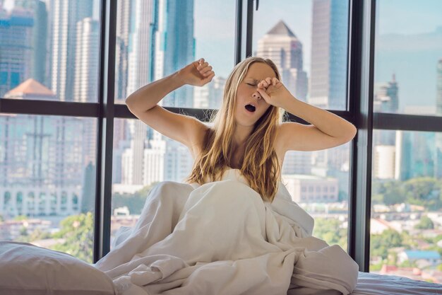 Vrouw wordt 's ochtends wakker in een appartement in de binnenstad met uitzicht op de wolkenkrabbers. Leven in het rumoer van het grote stadsconcept. Niet genoeg slaap