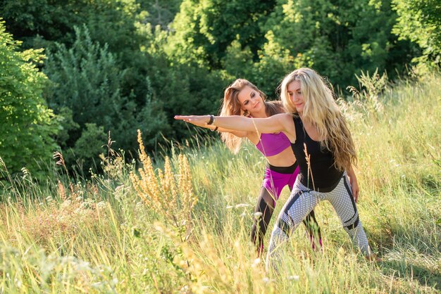 Vrouw yoga-instructeur lesgeven aan beginner in de natuur op een zonnige dag