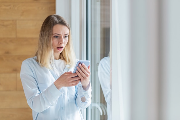 vrouw zag slecht nieuws op smartphone bij het raam op kantoor of thuis