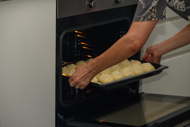 vrouw zet broodjes in de oven op een bakplaat 2