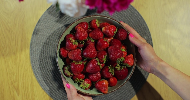 Vrouw zet een kom rijpe aardbeien op tafel Zomerbessenoogst