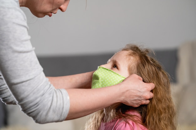 Vrouw zet herbruikbaar beschermend masker op kind tijdens pandemie van virus.