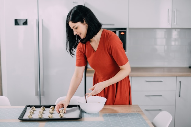 Vrouw zet op bakplaat rauwe koekjes voor het bakken in de keuken